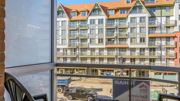 Uitzicht vanaf een balkon op een meerlaags gebouw met balkons en een straat eronder.