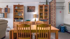 Een eethoek met een houten tafel en stoelen, omringd door houten kasten en planken met diverse spullen.