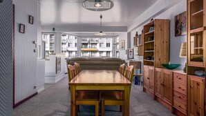 Een eetgedeelte met een houten tafel en stoelen, een bank en houten kasten met planken.