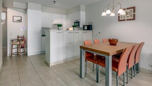 A modern kitchen with white cabinets, a wooden dining table with orange chairs, and a hanging light fixture.