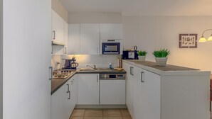 A compact kitchen with white cabinets, a microwave, a dishwasher, and a sink. There are two potted plants on the countertop.