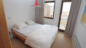 Um quarto com cama, janela e vista para edifícios lá fora.