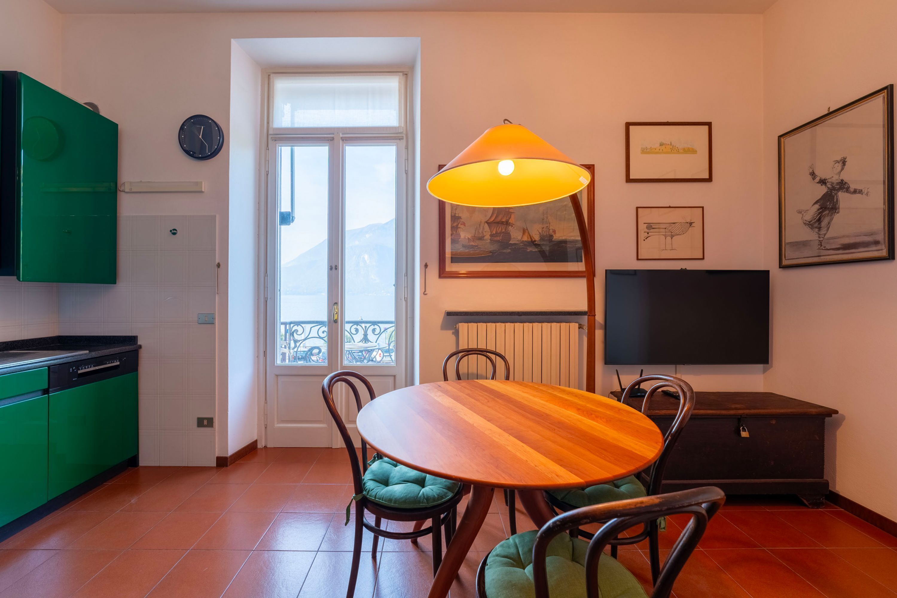 Un comedor con mesa y sillas de madera, un sofá verde, un televisor y obras de arte en las paredes.