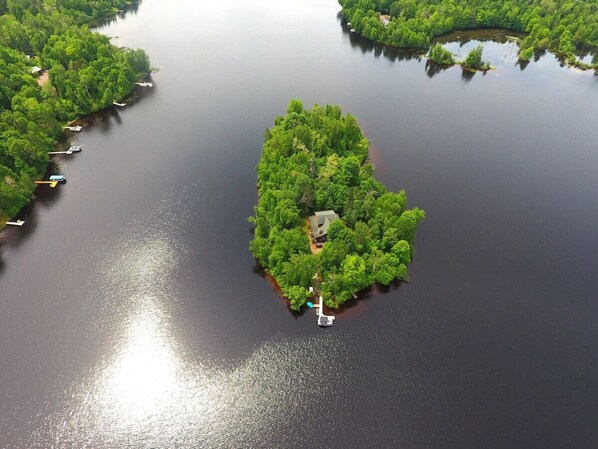 Vista aerea di una piccola isola ricca di vegetazione, alcune barche e una casa circondata da alberi.