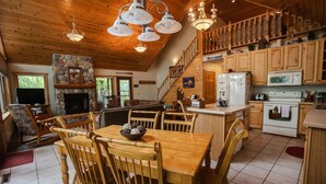A spacious kitchen with wooden cabinets, a stone fireplace, and a dining area with wooden chairs and a table. - Private Island on Lake Winter (Winter)