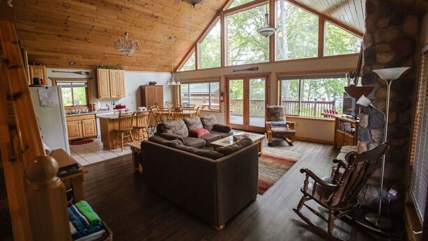 A spacious living area with a large couch, wooden flooring, and a stone fireplace. - Private Island on Lake Winter (Winter)