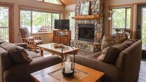 A cozy cabin interior with a stone fireplace, wooden ceiling, and large windows. - Private Island on Lake Winter (Winter)