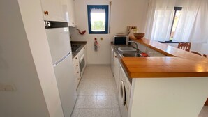 Une cuisine compacte avec des meubles blancs, un four encastré, un four à micro-ondes, un évier et un plan de travail en bois.