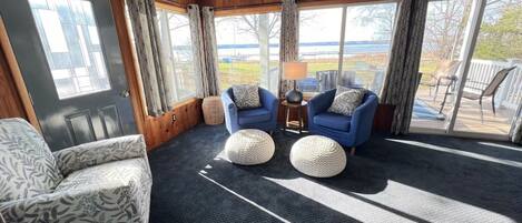 Ein Zimmer mit zwei blauen Sesseln, einem gemusterten Sofa und einem großen Fenster mit Vorhängen.