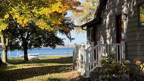 A wooden cabin with a white railing and a red door, located near a body of water.