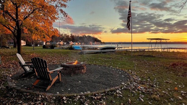 A lakeside outdoor seating area with Adirondack chairs, a fire pit, and a dock extending into the water.