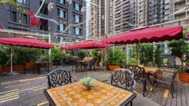 An outdoor patio area with tables and chairs, red umbrellas, and potted plants. - James Joyce Coffetel (Chengdu)