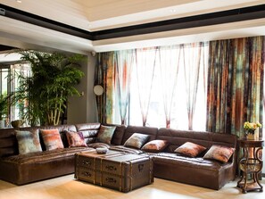 A spacious living room with a large sectional sofa, a vintage suitcase, and a large window with colorful curtains. - James Joyce Coffetel (Chengdu)