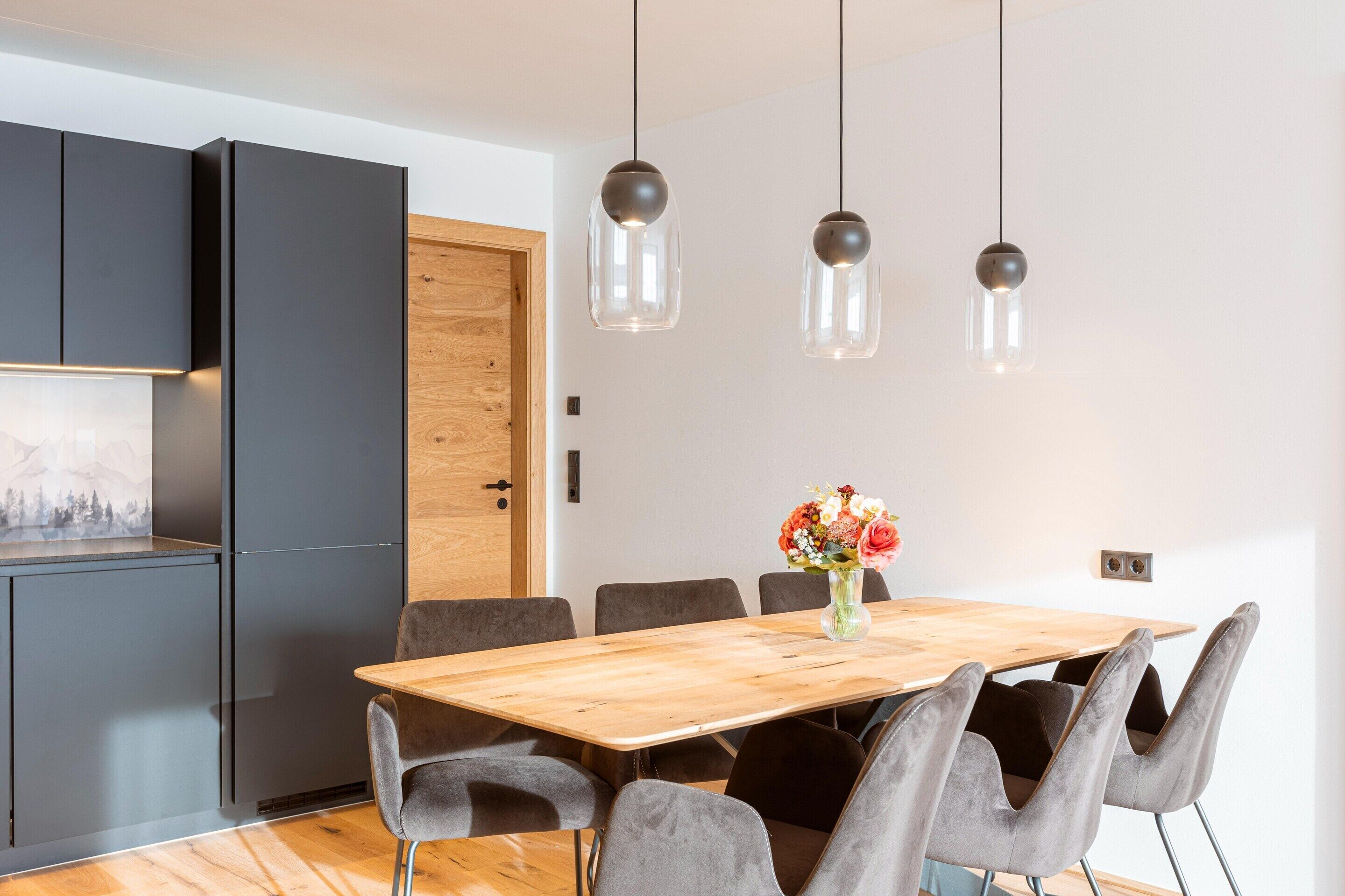 A modern dining area with a wooden table, grey upholstered chairs, and pendant lighting.