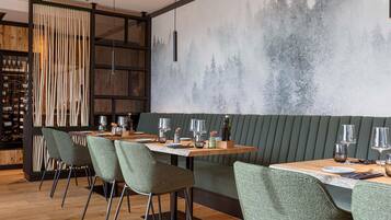Un restaurante con una larga mesa de madera, sillas tapizadas de verde y un mural en la pared que muestra un bosque.