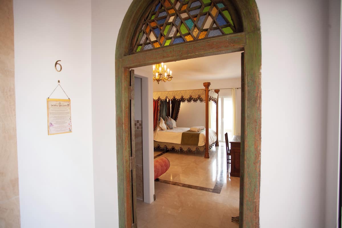 A bedroom with a four-poster bed, a chandelier, and a door with a number '6' sign.