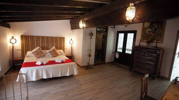 A bedroom with a large bed, wooden beams, a dresser, and two wall-mounted lamps.