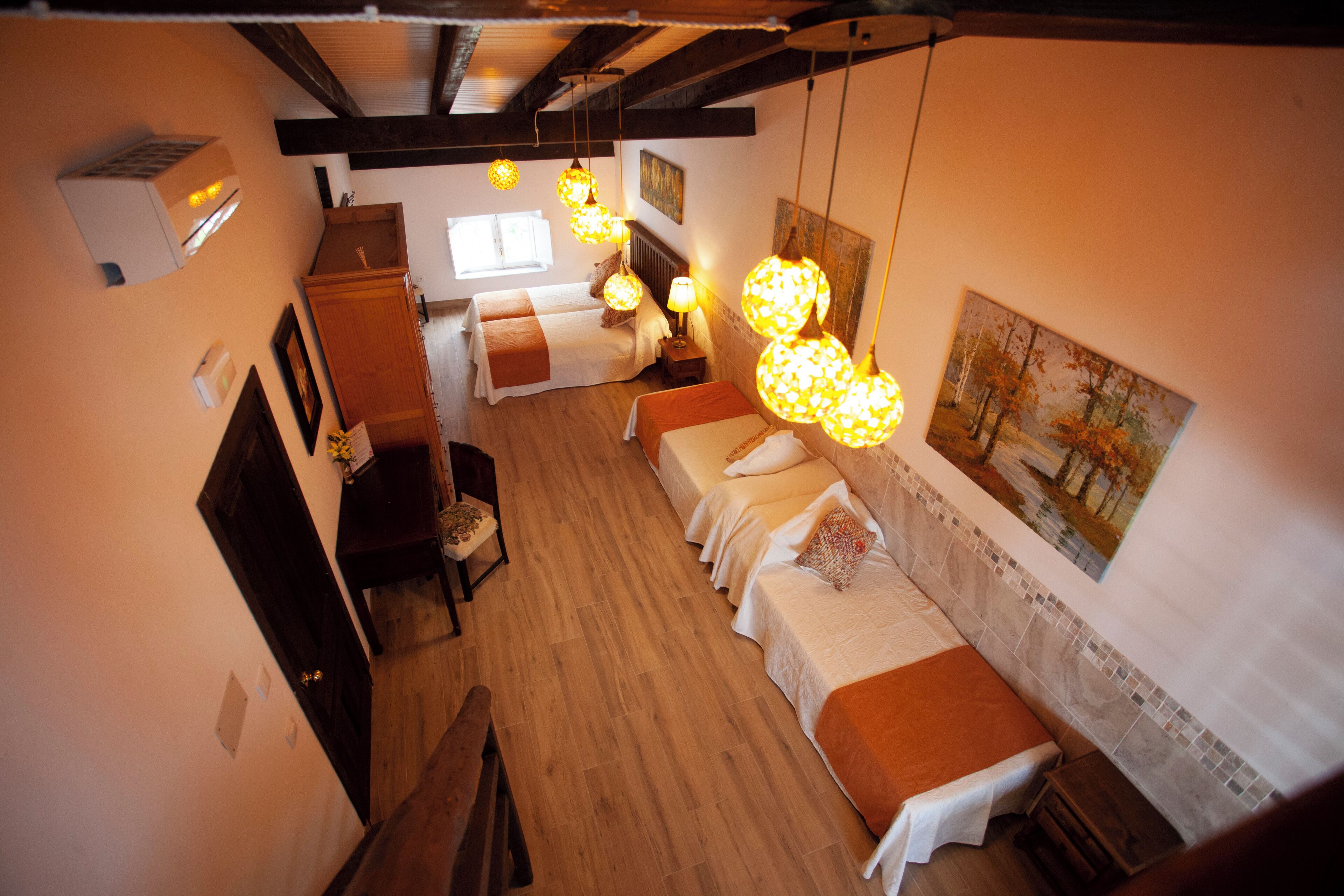 Habitación de hotel con piso de madera, cama con cubrecama blanco, mesita de noche con lámpara y un cuadro en la pared.