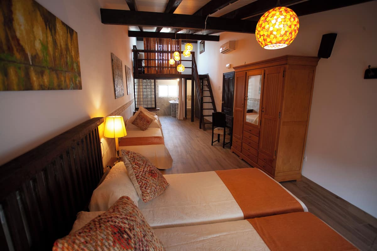 A bedroom with two beds, a wooden wardrobe, a staircase, and a hanging light fixture.