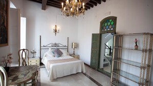Un dormitorio con cama, mesitas de noche, una araña, un espejo y una silla.