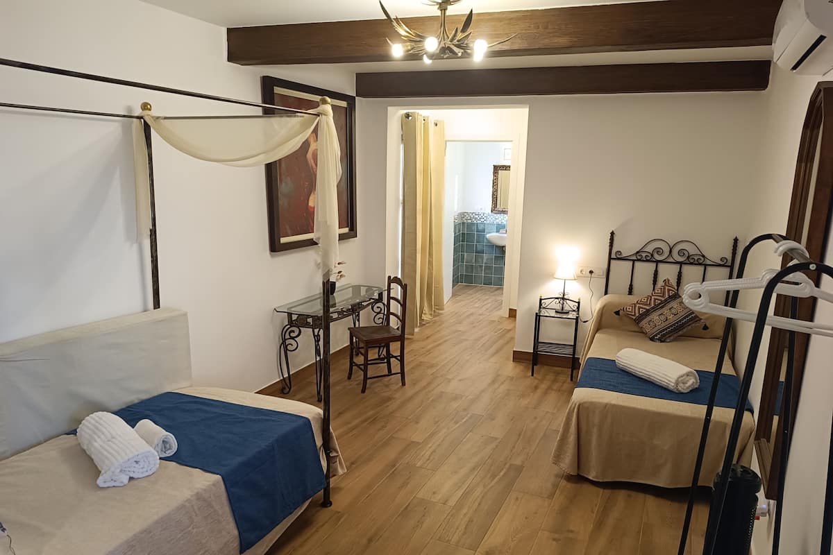 A room with two beds, a small table, a chair, and a ceiling fan.
