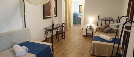 Ein Zimmer mit zwei Betten, einem kleinen Tisch, einem Stuhl und einem Deckenventilator.