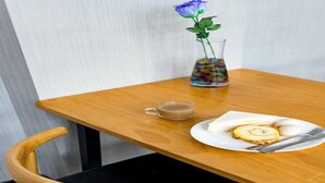 Un tavolo di legno con una tazza di caffè, un piatto con uova e una fetta di torta, e un vaso con una rosa blu.