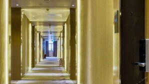 Un lungo e stretto corridoio d'hotel con pavimento rivestito di moquette e pareti in legno.