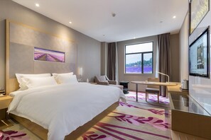 A hotel room with a large bed, a desk, a chair, a TV, and a window with a view of lavender fields. - Lavande Hotel (Guangzhou)