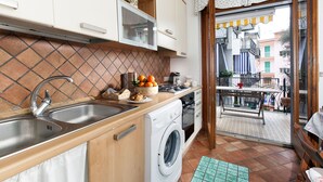 Une cuisine compacte équipée d’un lave-linge, d’un évier et d’une fenêtre donnant sur un balcon.