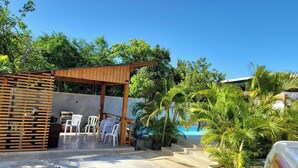 A covered outdoor seating area with chairs and a wooden pergola, surrounded by lush greenery and a pool. - Room-serene Punta Cana Cabin Retreat - P (Punta Cana)