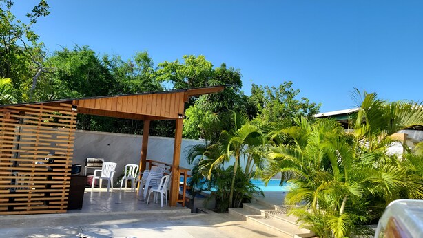 An outdoor patio area with a wooden pergola, white plastic chairs, and a pool. - Room-serene Punta Cana Cabin Retreat - P (Punta Cana)