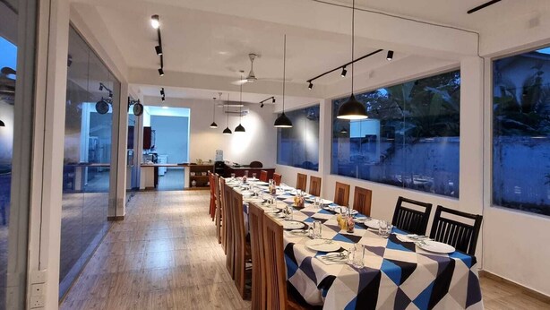 A modern dining area with a long table set for a meal, large windows, and a view of the outdoors. - Utopia Polhena Hotel (Matara)