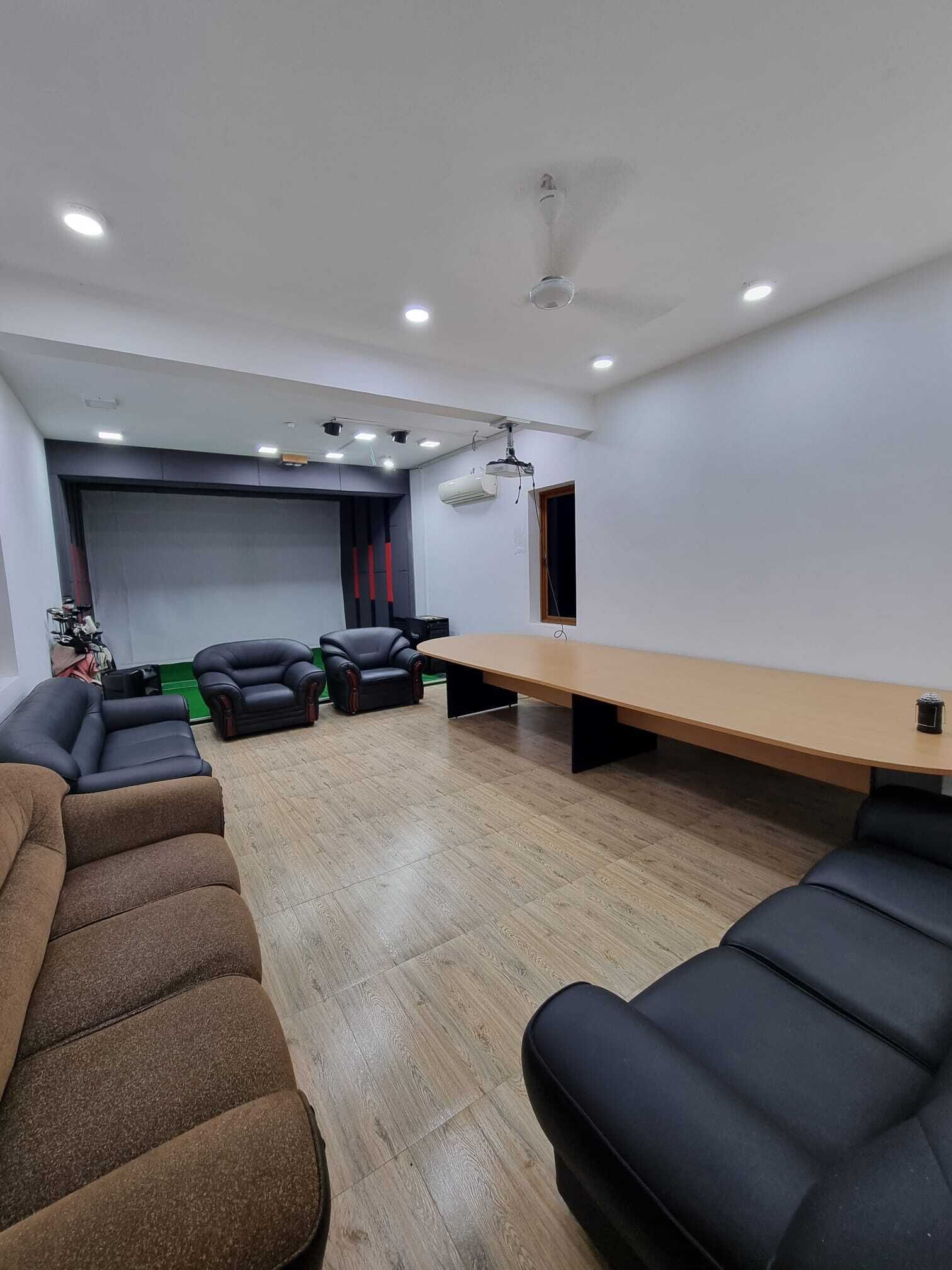 Une salle de conférence avec une longue table, des fauteuils en cuir noir, un projecteur et un ventilateur de plafond.