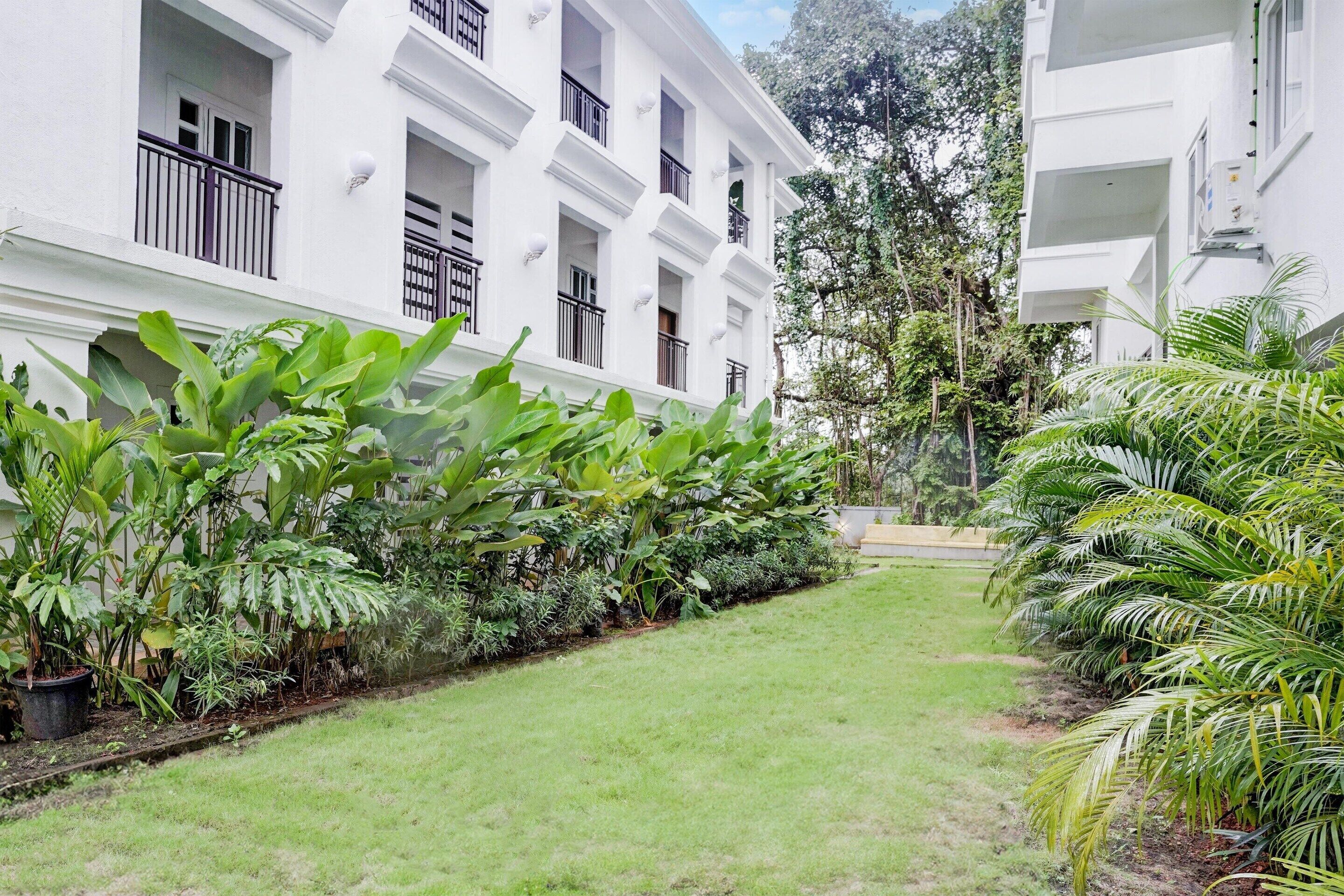 Um edifício branco com várias varandas e um jardim bem cuidado com diversas plantas.