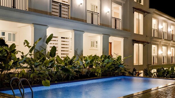 A swimming pool with a clear blue edge, surrounded by lush green plants. - Sereno By Dancenter 1bhk Apartment In Siolim (Siolim)