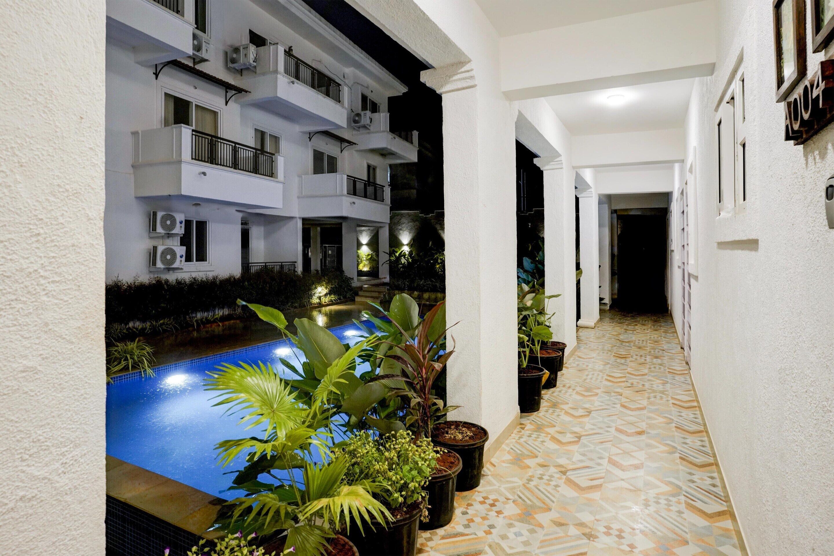 Corridoio di un hotel con piscina, piante in vaso e pavimento piastrellato.