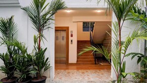 A hotel entrance with potted plants, a wooden staircase, and an elevator. - Sereno By Dancenter 1bhk Apartment In Siolim (Siolim)