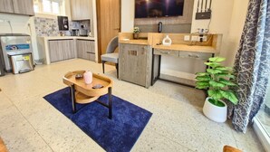 A modern kitchen with a built-in oven, a dining area with a blue rug, and a large TV mounted on the wall. - Sereno By Dancenter 1bhk Apartment In Siolim (Siolim)