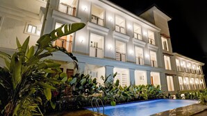 A multi-story hotel with balconies, a swimming pool, and lush greenery. - Sereno By Dancenter 1bhk Apartment In Siolim (Siolim)