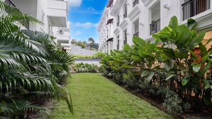 A courtyard with a well-maintained lawn, surrounded by white buildings with balconies and windows. - Sereno By Dancenter 1bhk Apartment In Siolim (Siolim)