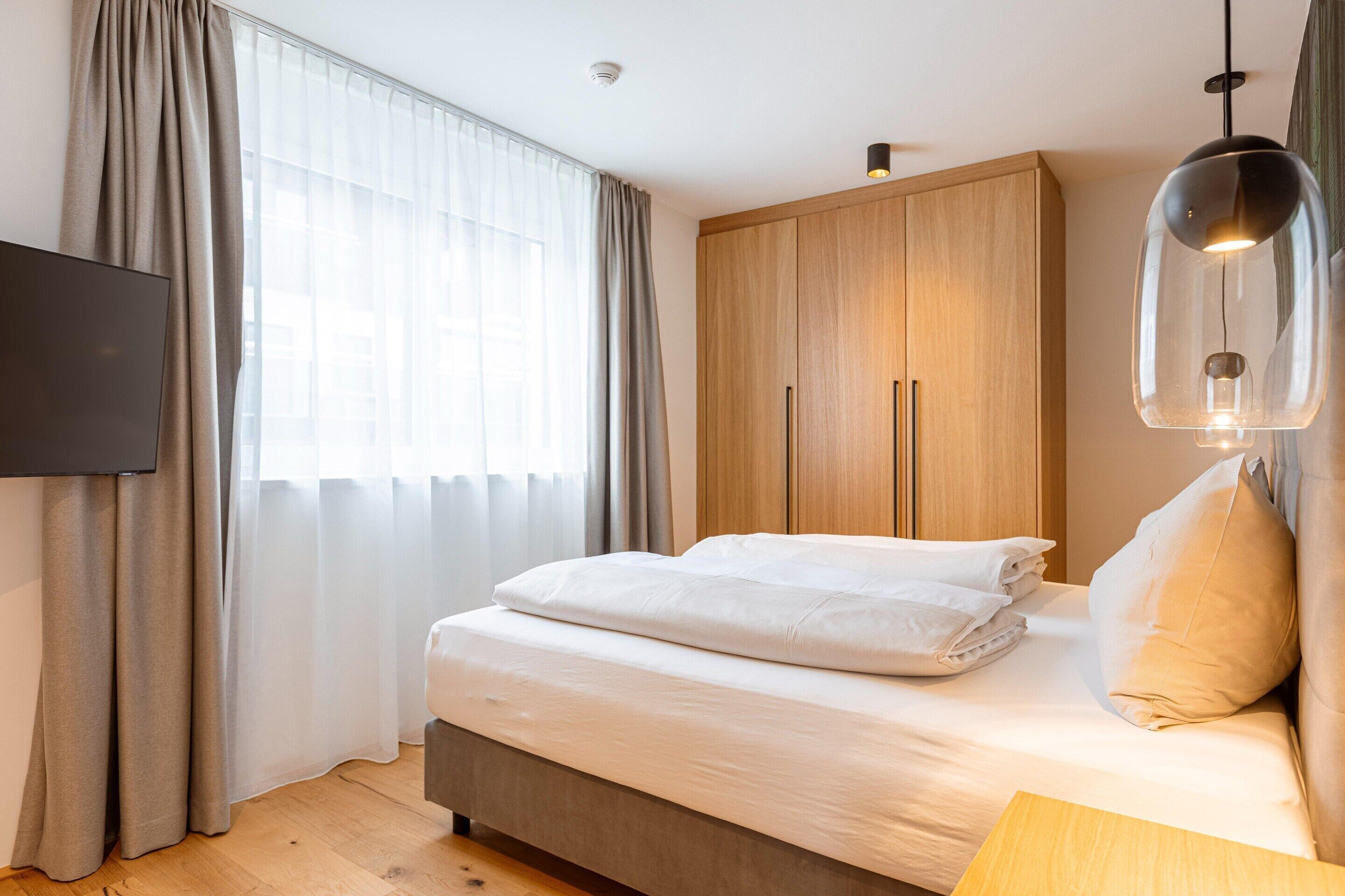 A bedroom with a bed, a wardrobe, a television, and a window with curtains.