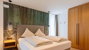 Un dormitorio con cama, mesita de noche, armario y pared con un mural de un bosque.