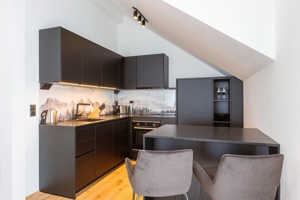 A modern kitchen with dark cabinetry, a built-in oven, and a dining area with two chairs.