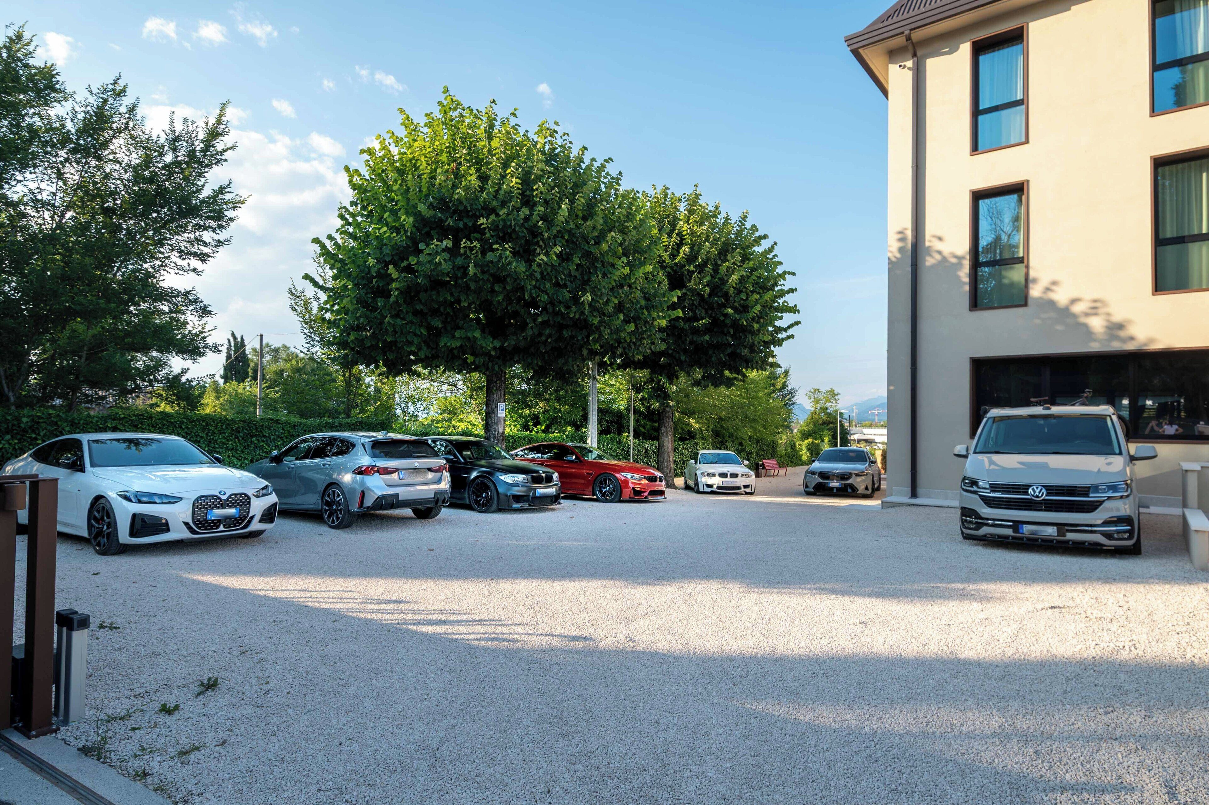 A parking area with multiple cars, a building with large windows, and a tree in the background.