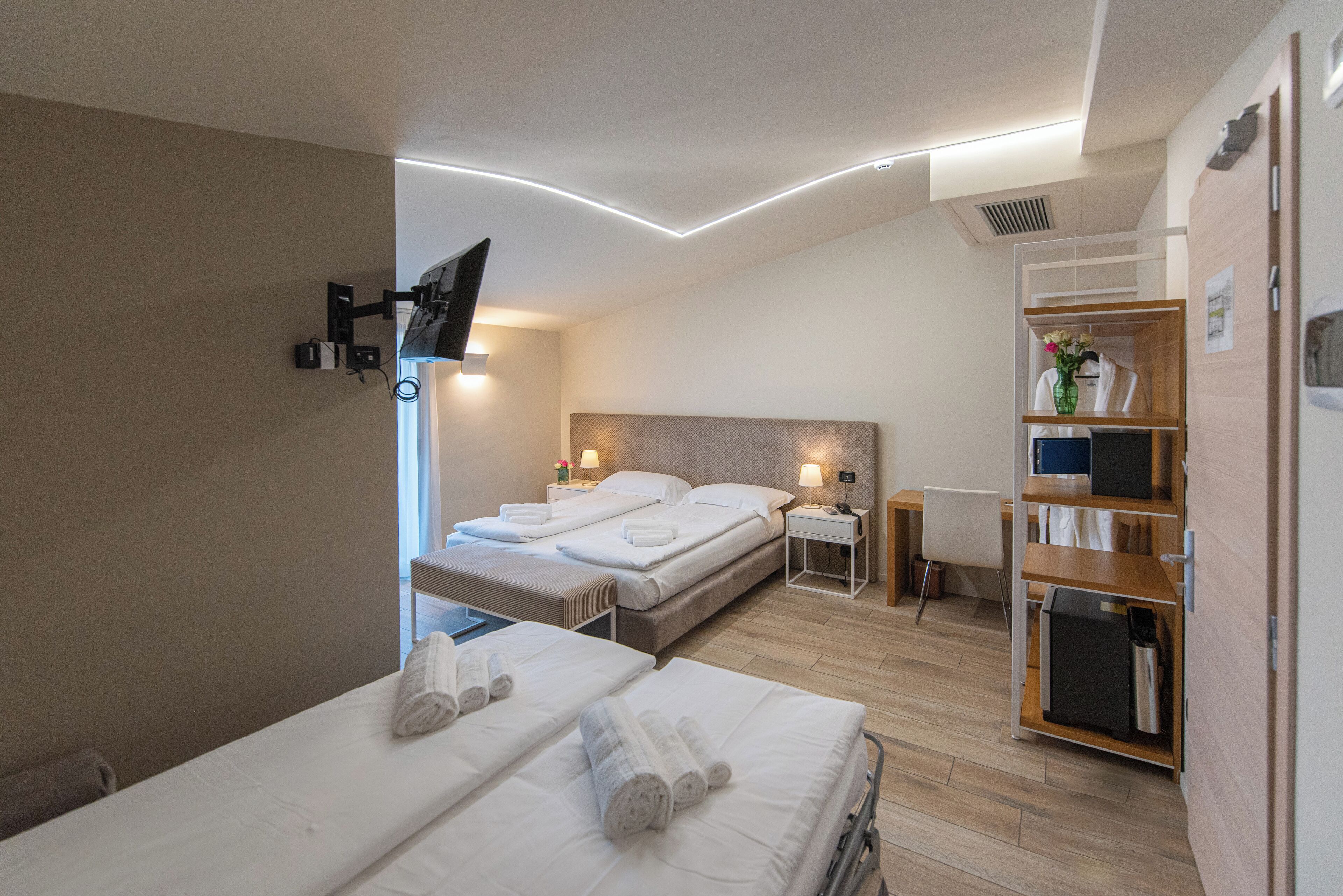 A hotel room with two beds, a desk, a chair, a TV mounted on the wall, and a built-in bookshelf.
