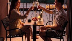 A couple toasting with champagne glasses at a table with a view of trees and a sunset.