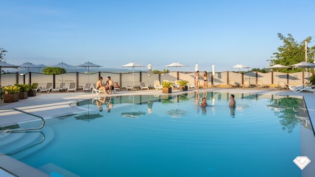 A swimming pool with lounge chairs and umbrellas, surrounded by a low wall and potted plants.