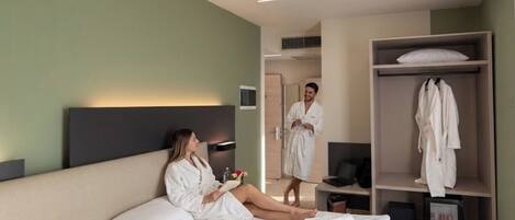 A modern hotel room with a large bed, a bedside table, a robe hanging on a rack, and a mirror.