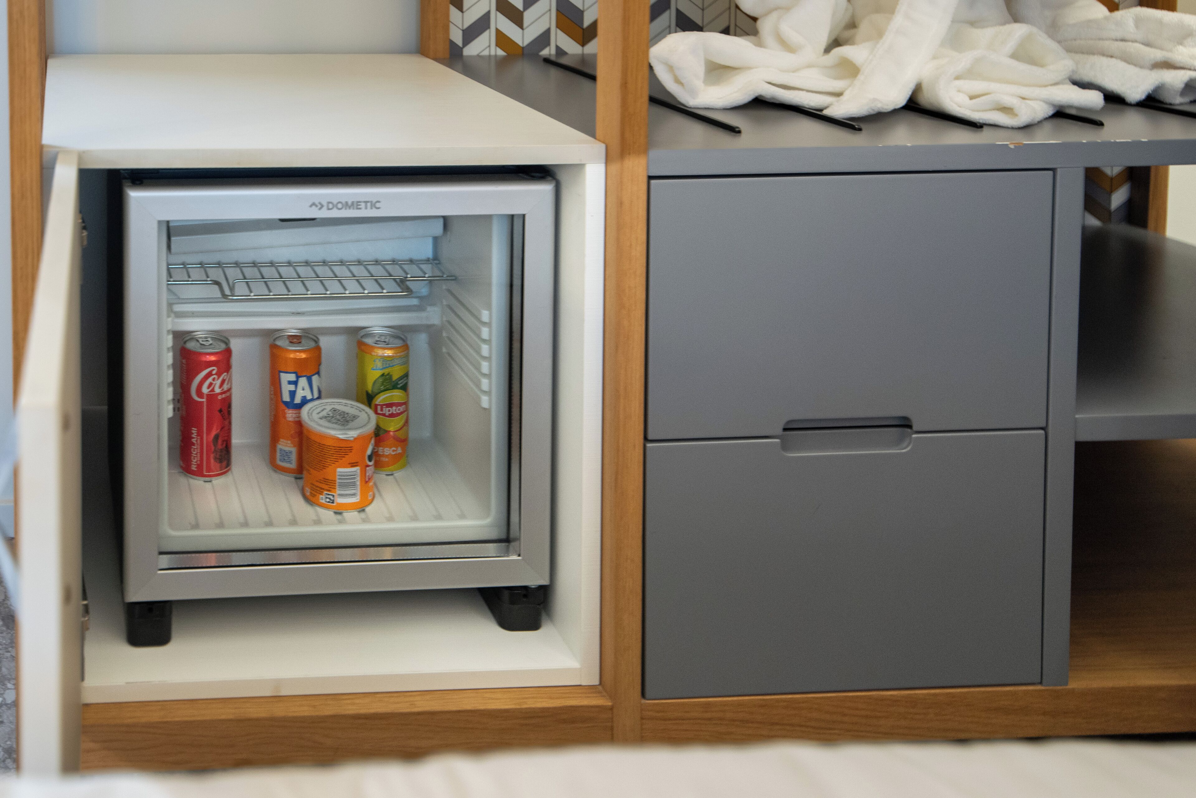 A mini-fridge with beverages and a grey cabinet.